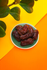 Close-up of Dates fruit in ceramic plate on color paper background with empty space for your text or message. healthy food concept.