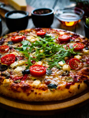 Pizza with goat cheese, tomatoes, olives, parmesan and mozzarella on wooden table
