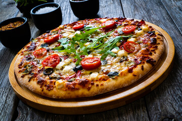 Pizza with goat cheese, tomatoes, olives, parmesan and mozzarella on wooden table
