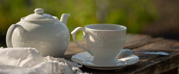 Elegant cup, lace tablecloth, teapot, wooden table. Outdoor breakfast, picnic, brunch, spring mood. Soft focus