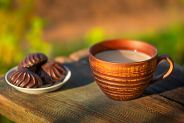 Pottery cup with milk (kefir, yogurt, sour cream, kumis), marshmallow, wooden table. Outdoor...