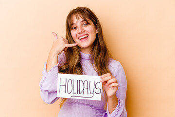 Fototapeta na wymiar Young caucasian woman holding a Holidays placard isolated showing a mobile phone call gesture with fingers.
