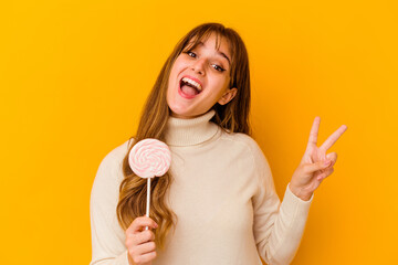 Young caucasian woman holding a lollipop isolated on yellow background joyful and carefree showing...