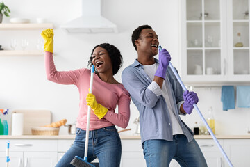 Happy african american lovers singing songs while house-keeping in kitchen
