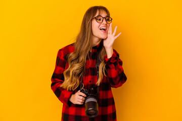 Young photographer caucasian woman isolated on yellow background shouting and holding palm near opened mouth.