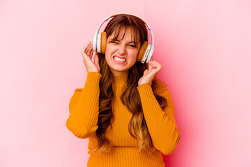 Young caucasian woman listening music with headphones isolated covering ears with hands.