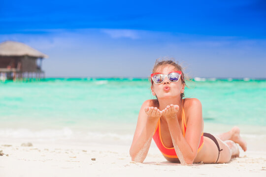long haired woman in bikini and straw hat blowing a kiss on tropical beach