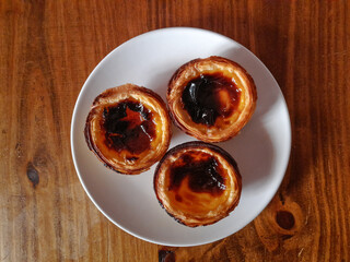 Portuguese Custard Tarts in a plate on a wooden table	
