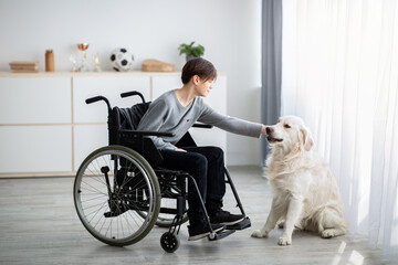 Full length of handicapped teenage boy in wheelchair petting his dog at home. Animal-assisted therapy concept
