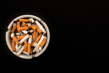 Ashtray with cigarette butts. Full of ashes. On a black background. Place for your text.
