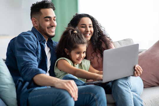 Young Arabic Parents And Their Little Girl Relaxing With Laptop At Home