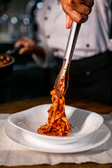 pasta being placed on the plate with a tongs by the chef
