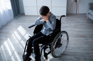Above view of handicapped adolescent in wheelchair crying at home. Depression and loneliness in...