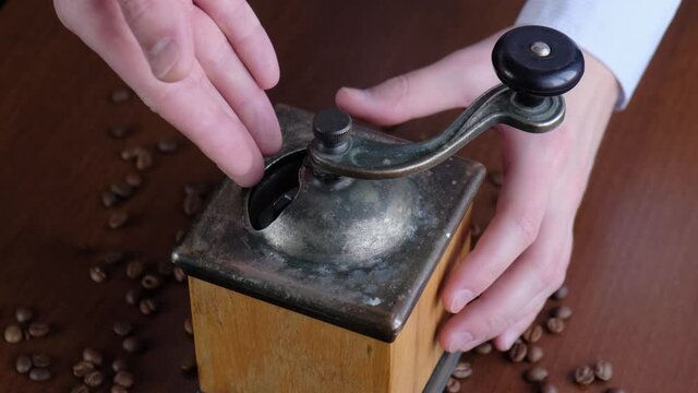 A man pours coffee beans into a coffee grinder, closeup
