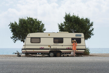Girl in a hat with a bag at the sea near the trailer, camper