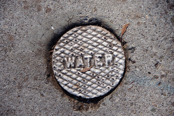 Small iron cover plate for a water valve in the asphalt of a city street 