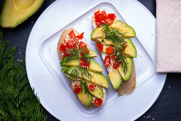 on a slice of baguette slices of fresh avocado and slices of ripe tomato, sprinkled with sesame seeds, on a white plate and a napkin