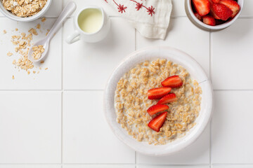 Simple oatmeal porridge with strawberries in a white plate on a linen napkin. Breakfast health food concept. Top view