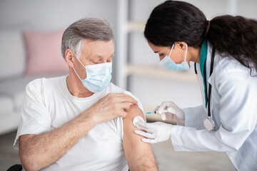 Immunizing homebound patients with covid-19 vaccine. Young doctor giving injection against covoravirus to elderly man - obrazy, fototapety, plakaty