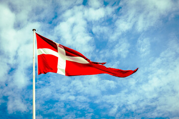 Danish Flag, the Dannebrog, in front of a blue and cloudy sky.