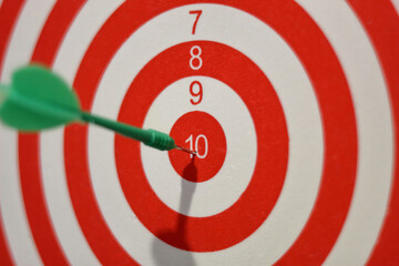 closeup of red and white dartboard with plastic green arrow in the middle