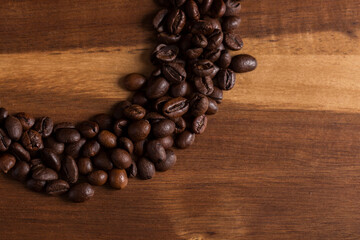 Roasted coffee beans making a circle on a wooden table.