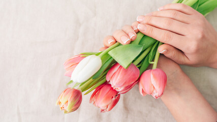 Close up hands of woman florist with flowers. Florist holding blooming bouquet of pink tulips on linen background. Flowershop concept. Happy woman's day mothers day. Copy space
