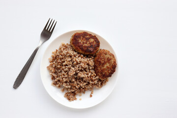 Garnish buckwheat porridge and meatballs on a plate on a white background. Home-cooked food. Top view, copy space