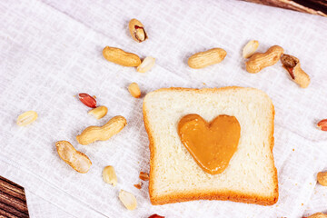 Homemade toasts for breakfast with fresh crunchy heart shaped peanut butter and nuts on light textile background.