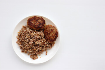 Garnish buckwheat porridge and meatballs on a plate on a white background. Home-cooked food. Top view, copy space
