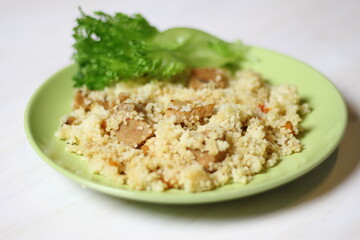 Cuscus with carrot, tomato, pork and salad leaf on green plate on white table