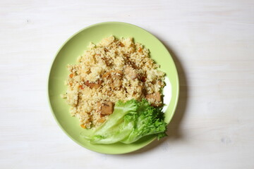 Cuscus with carrot, tomato, pork and salad leaf on green plate on white table