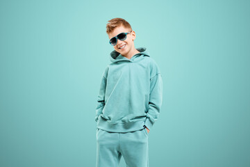 Little in a turquoise suit poses and fools around on a turquoise background, looks at the camera. Children's studio portrait. Childhood lifestyle concept.