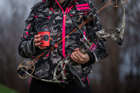 a woman in a camouflage suit with a professional bow drinks coffee