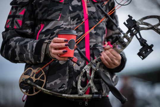 a woman in a camouflage suit with a professional bow drinks coffee