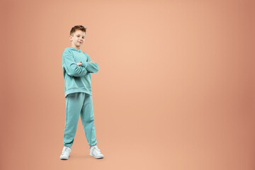Fototapeta na wymiar A boy in a turquoise suit posing and fooling around on a beige background, looking at the camera. Children's studio portrait. Childhood lifestyle concept.