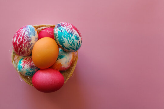 Happy Easter holiday! Colorful hand-painted Easter eggs in a decorative nest on pink background.