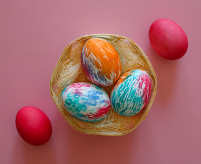 Happy Easter holiday! Colorful hand-painted Easter eggs in a decorative nest on pink background.
