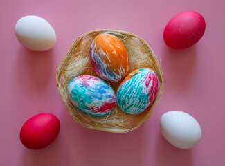 Happy Easter holiday! Colorful hand-painted Easter eggs in a decorative nest on pink background.