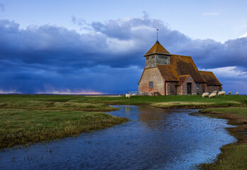 Saint Thomas Church near Fairfield on the Romney Marsh in Kent south east England, storm clouds gathering during blue hour and sheep grazing