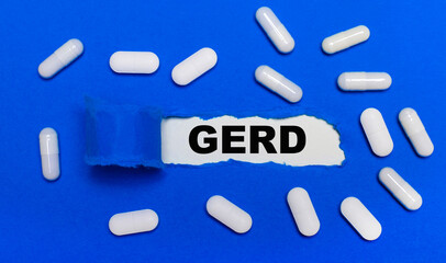 White pills lie on a beautiful blue background. In the center is white paper with the inscription GERD. Medical concept. View from above.