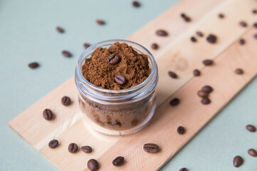 Body scrub from coffee in a glass jar on a light background on a wooden stand next to coffee beans and leaves, minimalism, vertical photo