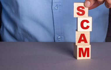 A man in a blue shirt composes the word SCAM from wooden cubes vertically