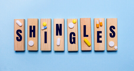 On a blue background, wooden blocks with word SHINGLES and pills. Medical concept
