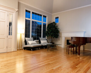 Modern living room with real oak hardwood floors, piano, fireplace and large windows during late...