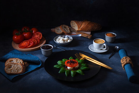 Variation of Caprese salad, slices of fresh ripe tomato, mini mozzarella, leaves of fresh basil and balsamic caviar..Dark background table.