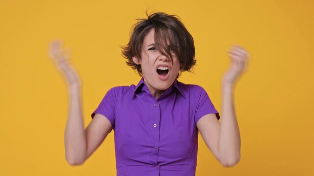 Angry mad sad nervous short hairdo young woman 20s years old in pink violet shirt look camera scream scolding protest waving hands ask what no tearing hair on head isolated on yellow background studio