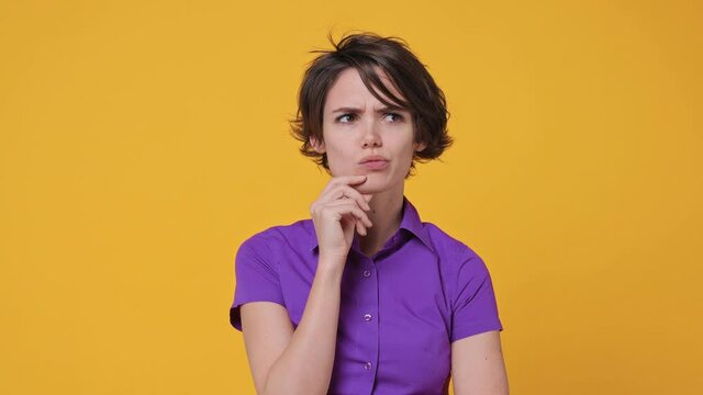 Insighted smart proactive short hairdo young woman 20s years old in pink violet shirt looks around thinks scratches at temple comes up with ideas raised finger up isolated on yellow background studio