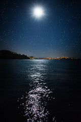 Fototapeta na wymiar Der Vollmond bei Nacht spiegelt sich auf dem Meer an einem Badeort auf Mallorca, Spanien.