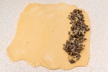 Yeast dough rolled out on the table, prepared for making patties with mushrooms.